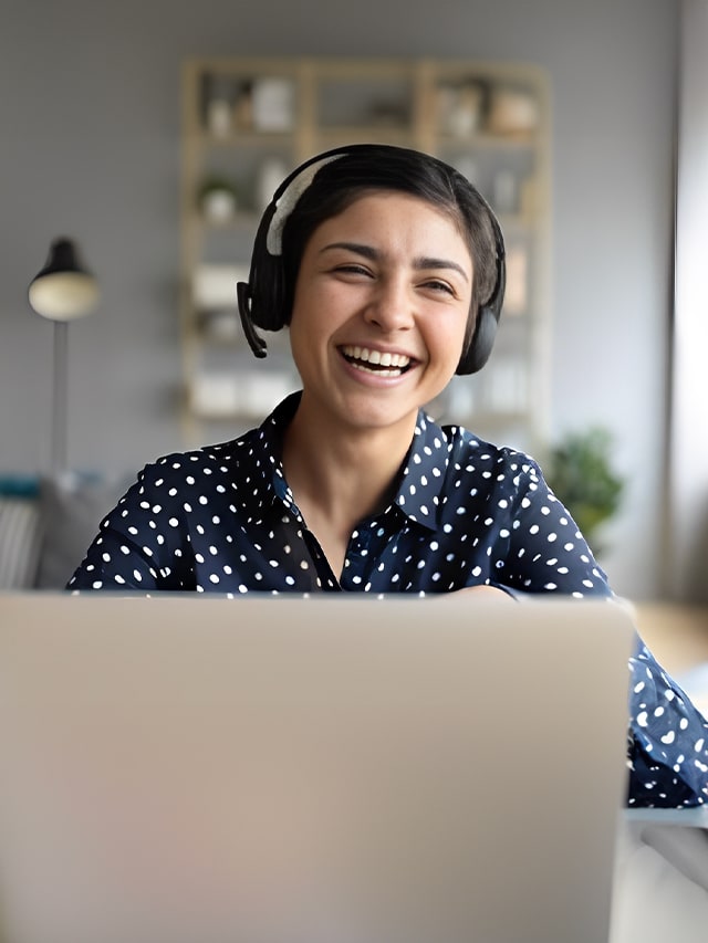 Cheerful indian woman working from home wearing headset using laptop video stream; work-from-home job concept