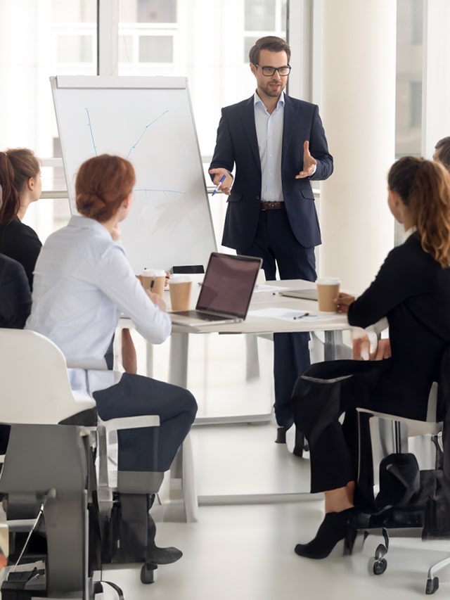 group of professionals gathered around a conference table with laptops and documents, engaged in discussion; concept of Job opportunities, career as a Sales Manager in top companies