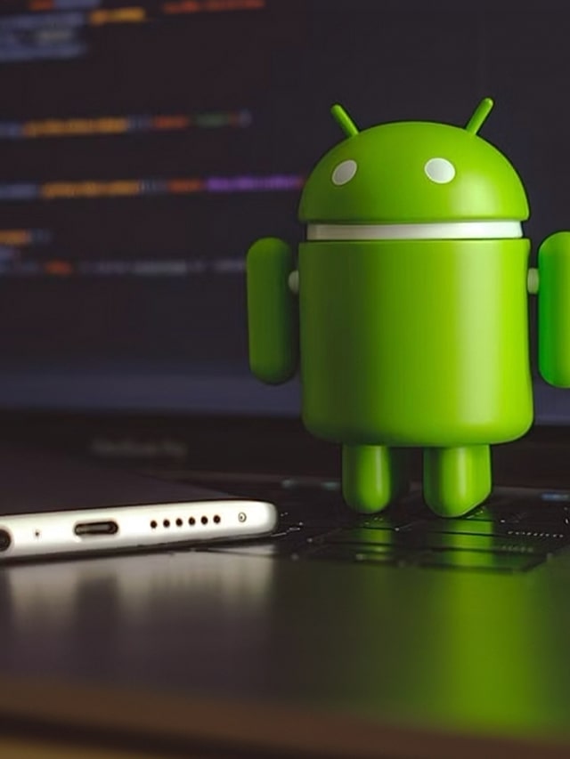 Google Android figure on a laptop keyboard next to a mobile phone, concept of Android Engineer jobs at Google Bangalore