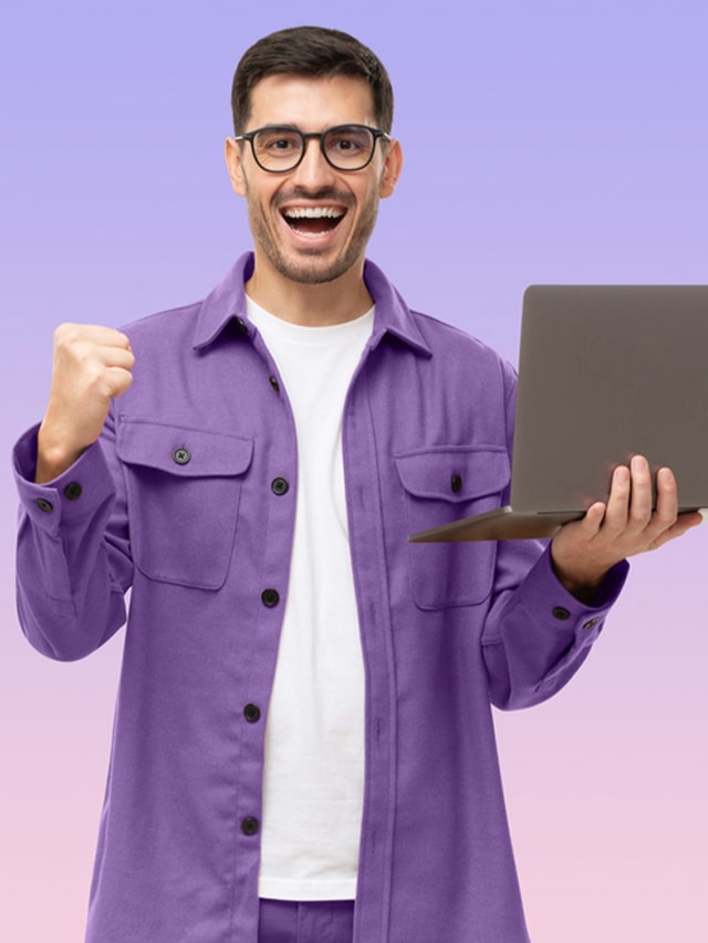 Happy young man in purple shirt looking at laptop screen with victory expression, isolated on purple background; concept of