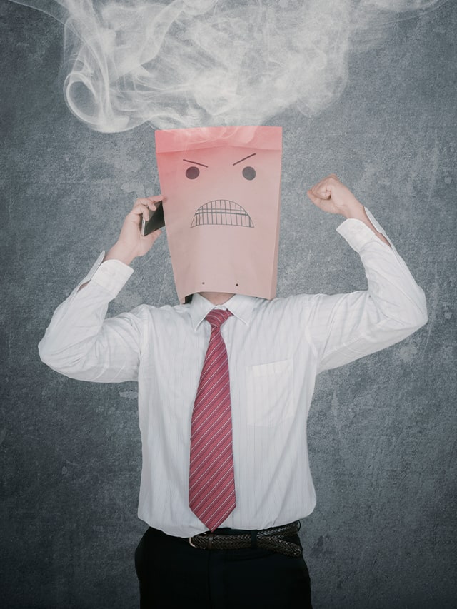 Midsection of man holding covering face against gray background; concept of How to Avoid Burnout at Work